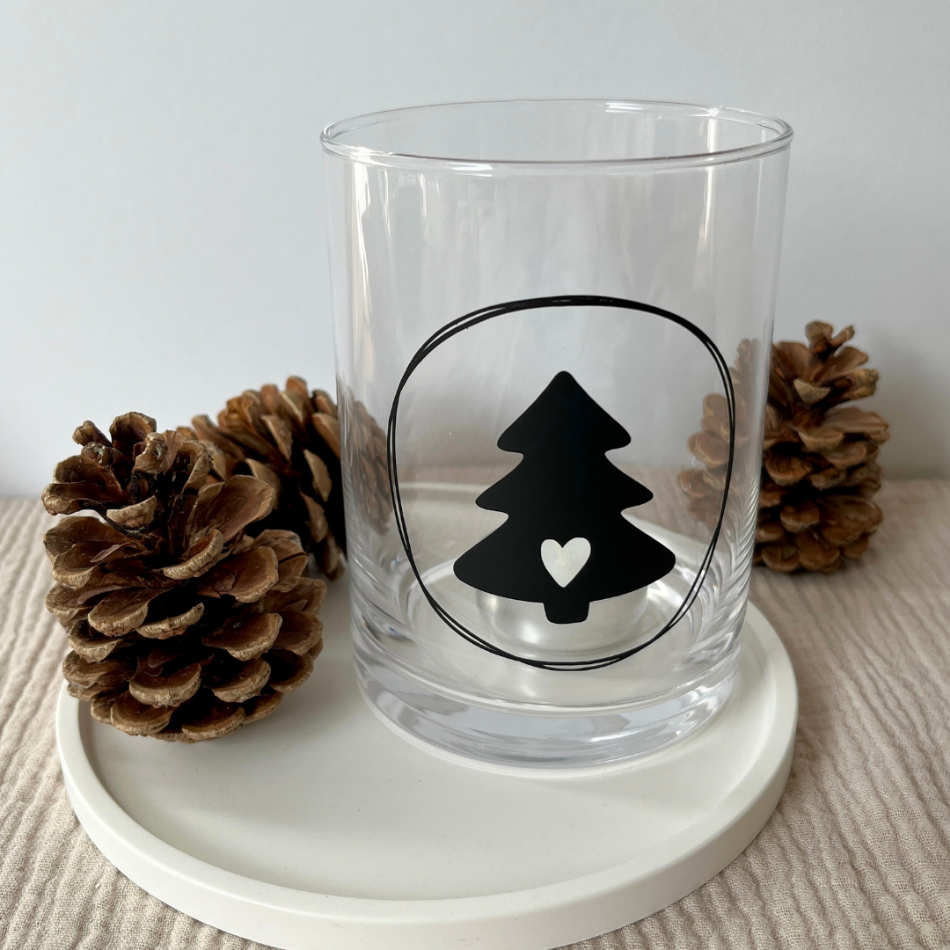 Tannenbaum mit Herz in der Mitte auf einem Kerzenglas und mit Tannenzapfen drumherum dekoriert.