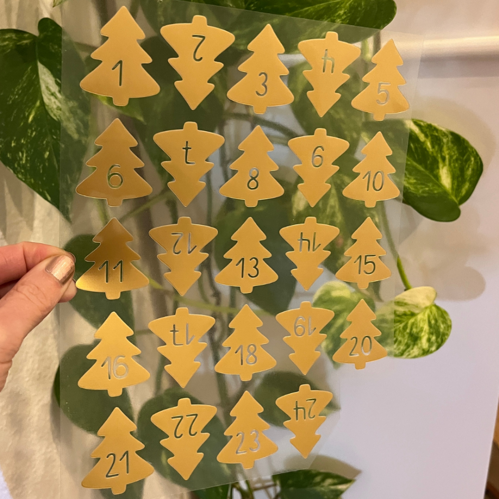 Aus goldener Folie geplottete Adventskalenderzahlen in Form von Tannenbäumen.