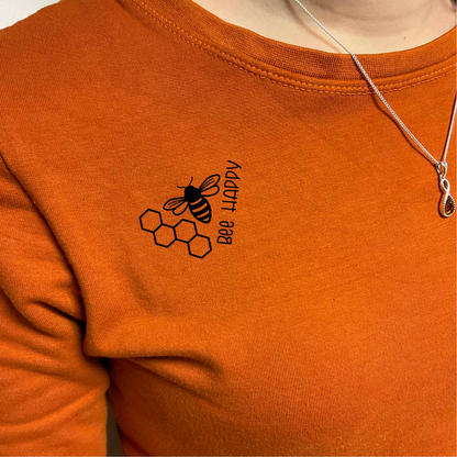 Schwarze Biene mit "bee happy" und Bienenwabe auf ein dunkelorangenes Sweatshirt gebügelt.