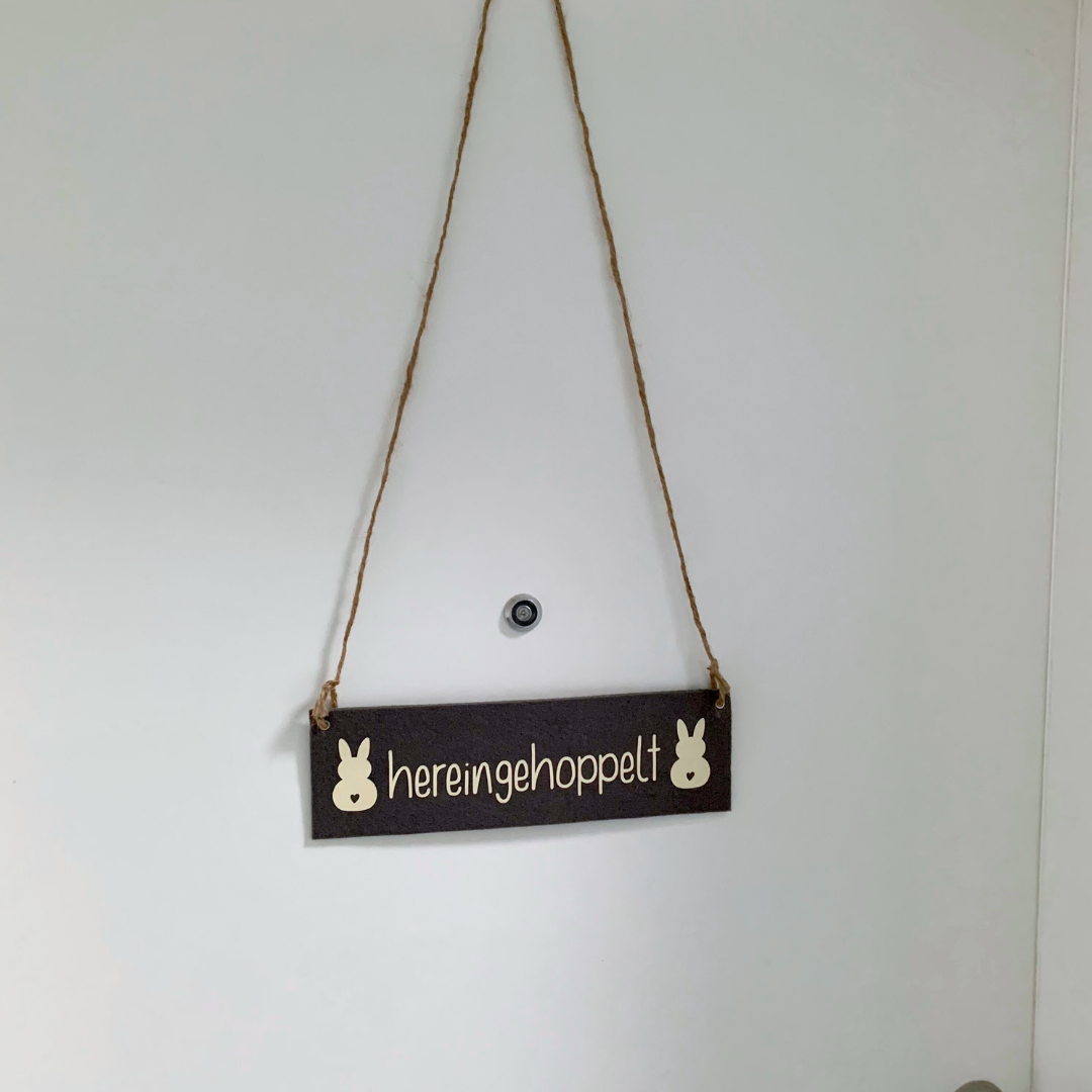 Türschild mit der geplotteten Aufschrift "hereingehoppelt" und zwei Osterhasen daneben.