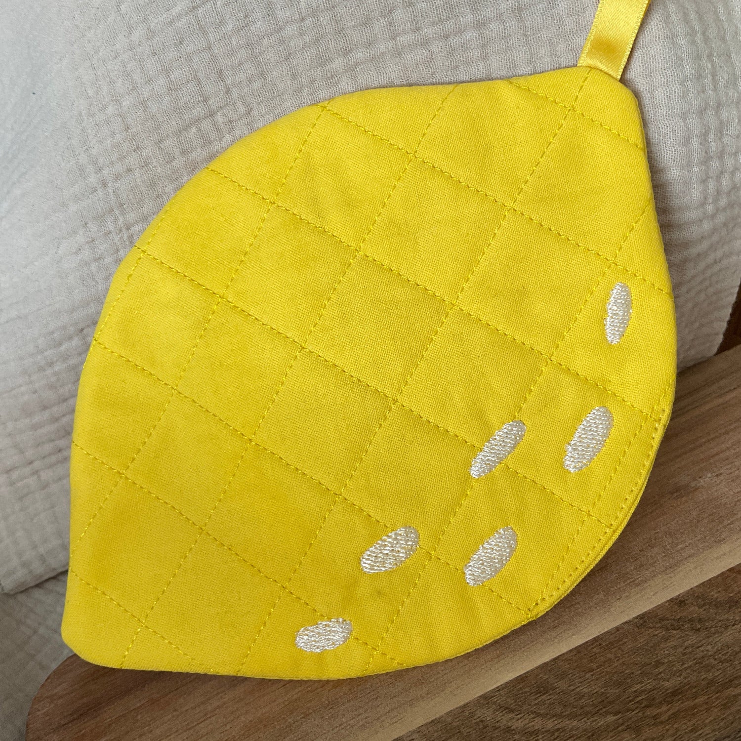 Fertig gestickter Topflappen in Form einer Zitrone. Gelber, gesteppter Stoff mit weißen, aufgestickten Schatten.