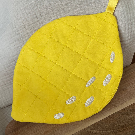 Fertig gestickter Topflappen in Form einer Zitrone. Gelber, gesteppter Stoff mit weißen, aufgestickten Schatten.